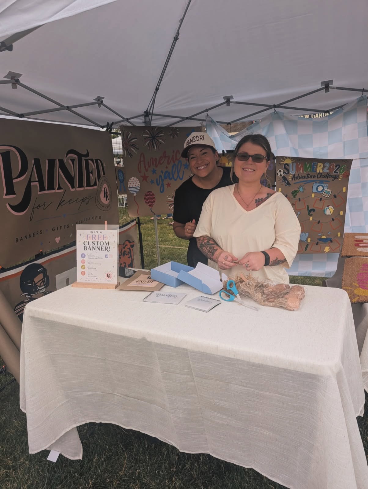 Brooke at her Painted for Keeps booth at a local market, surrounded by her hand-painted banners